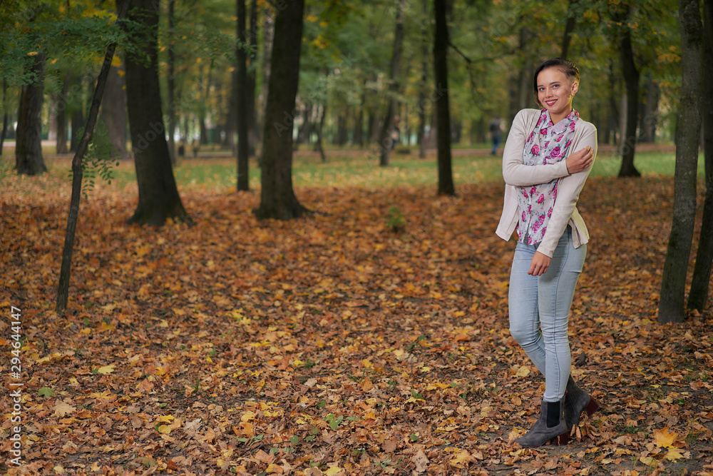 Autumn woman with a short haircut in jeans and a light autumn blouse in the park among fallen autumn leaves