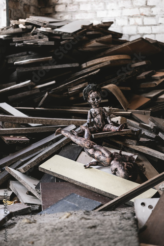 selective focus of abandoned and scary baby doll near damaged toy and wooden boards, post apocalyptic concept