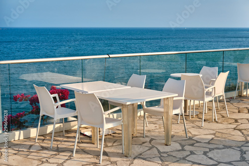 Restaurant terrace of a hotel with white table and chairs. Sea coast  white stone cape in Kalymnos island or Governor Beach in Cyprus.