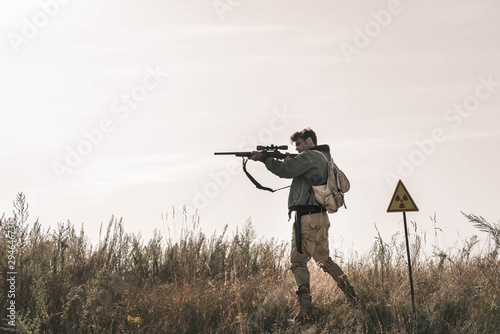 handsome man holding gun near toxic symbol in field, post apocalyptic concept