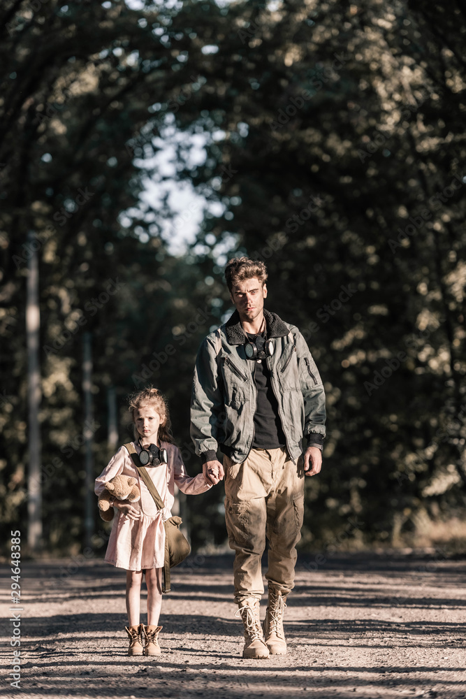 Fototapeta premium cute kid holding hands with man while holding teddy bear, post apocalyptic concept