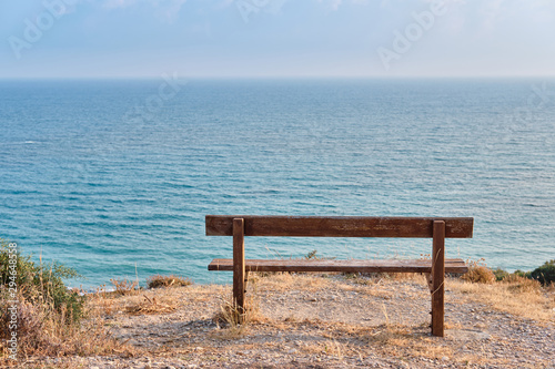 Close-up shot of a wooden bench standing on a mountain at the beach of azure mediterranean sea and surrounded by a beautiful nature of Cyprus.