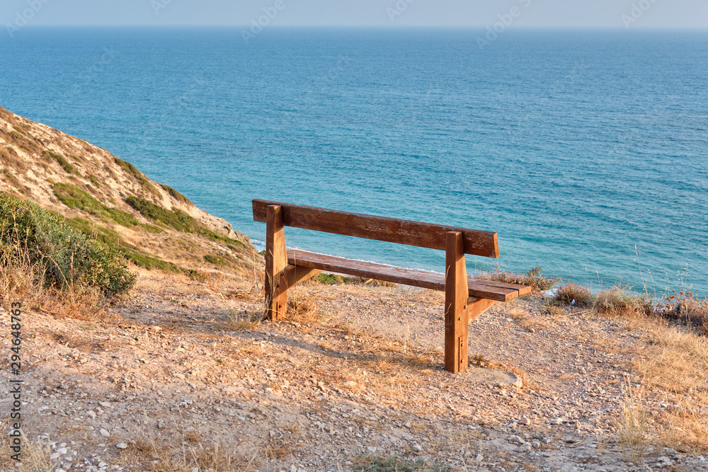Close-up shot of a wooden bench standing on a mountain at the beach of azure mediterranean sea and surrounded by a beautiful nature of Cyprus.