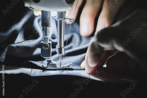 Hand of the seamstress is using a white industrial sewing machine to sew black cloth.