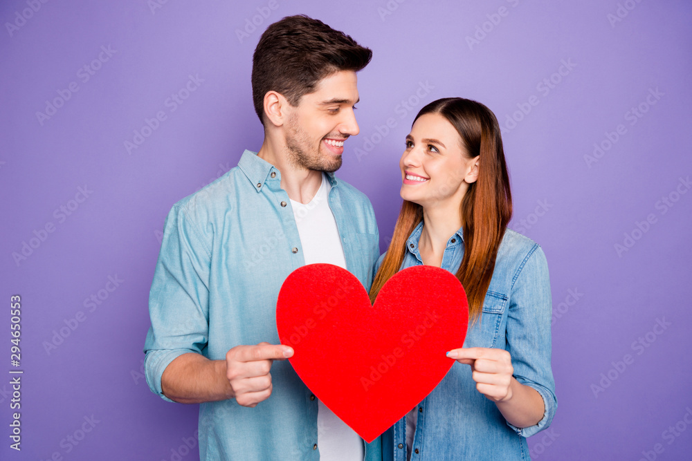 Portrait of romantic lovely spouses students hold paper card red big heart sign of their romance enjoy date 14-february holidays wear denim jeans shirt isolated over purple violet color background