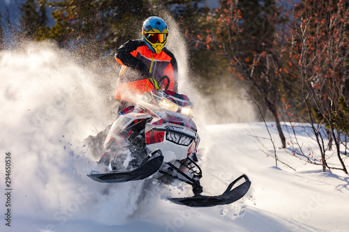 the guy is flying and jumping on a snowmobile on a background of winter forest  leaving a trail of splashes of white snow. bright snowmobile and suit without brands. extra high quality photo
