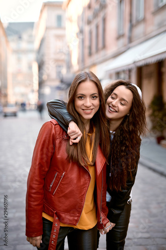 Lovable caucasian women in colored leather biker jackets and hoodies posing with smile on the street at autmn day.