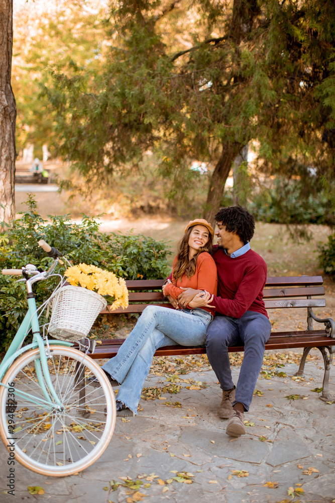 Multiratial loving couple sitting on bench in the autumn city park Multiratial loving couple sitting on bench in the autumn city park