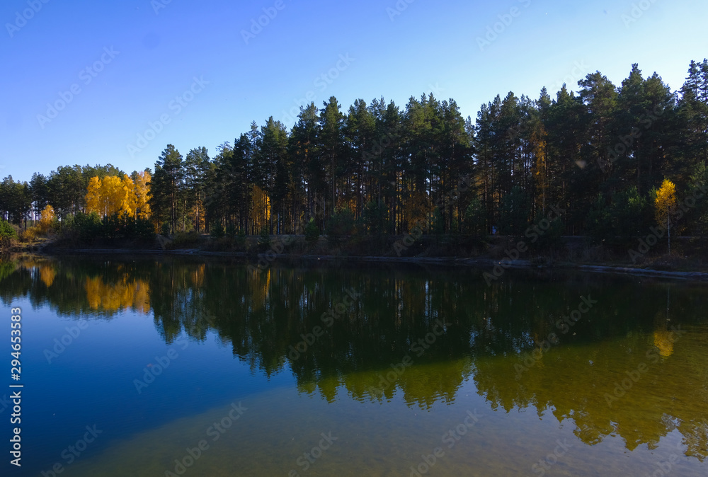 Lake in a delightful autumn forest at sunny day. Autumn trees with reflection. Russia. 
