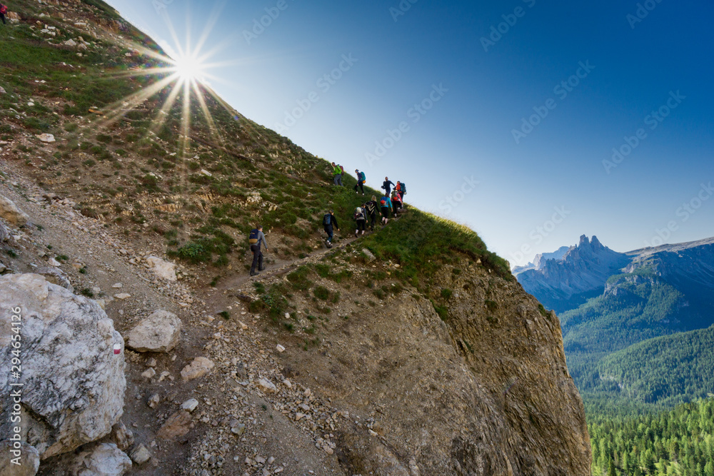 group of hikers on a steep hiking path in the Dolomites in Italy with the sun shining