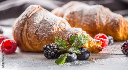 Freshly crispy croissants sprinkled sugar powder with raspberry blackberry and blueberry with mellisa leaves photo