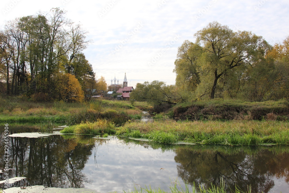 river in the village Dunilovo with church, houses, trees in autumn bright day
