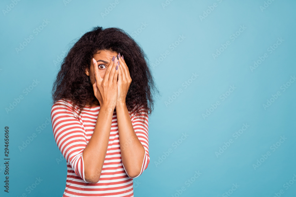 Photo of horrified scared black woan covering her face with hands hiding from danger looking through hand isolated over blue vibrant color background Photo of horrified scared black woan covering her face with hands hiding from danger looking through hand isolated over blue vibrant color background