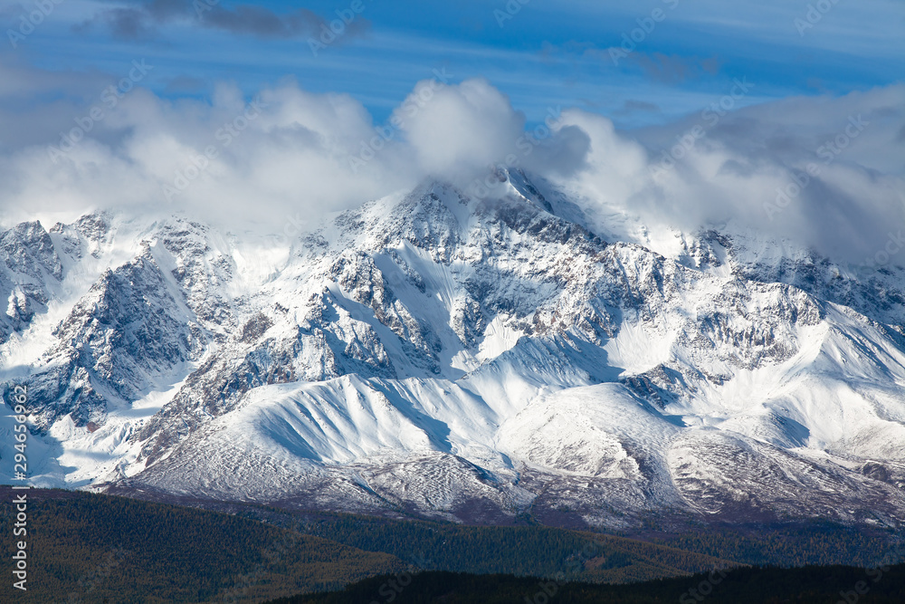 Scenery. Altai mountains. Snow-covered slopes of the North - Chuysky ridge. The tops of the mountains are covered with white clouds.