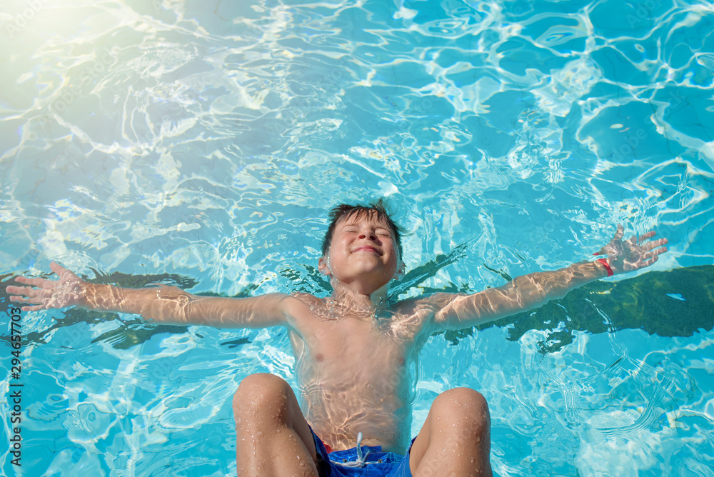 Portrait of cheerful European boy swimming in pool. He is enjoying his summer vacations.