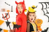 Young girl and boy in costumes holding paper cat and text Happy Halloween