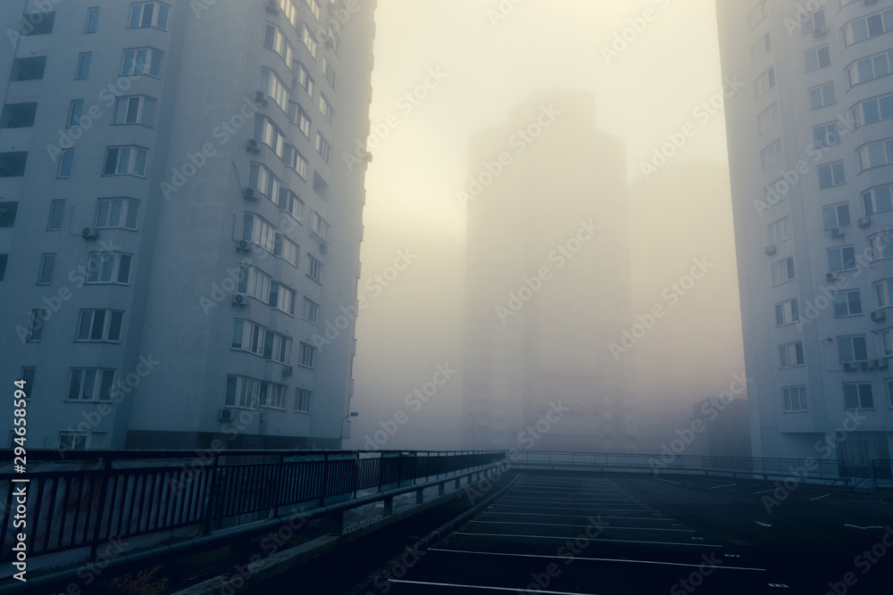 Obraz premium Empty parking space among residential buildings at modern urban district. Foggy morning with sunlight behind the scene.