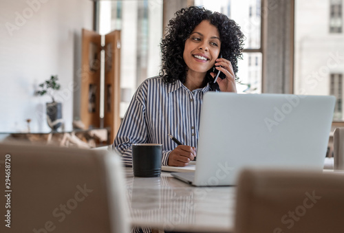 Smiling female entrepreneur sitting at home talking on her cellphone photo