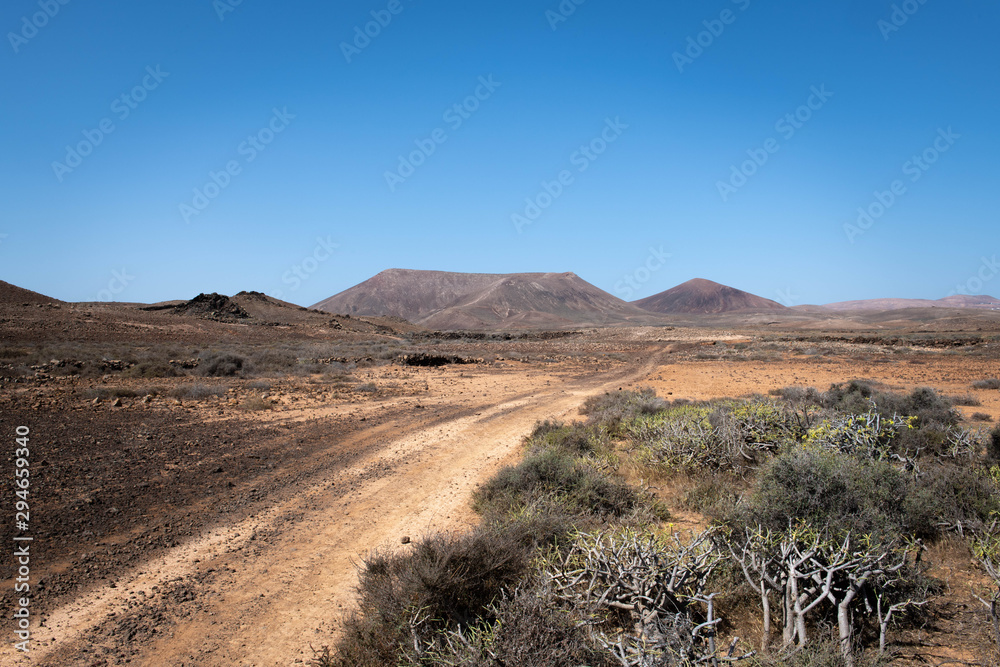 Dusty desert road on the canary island Lanzarote, with volcanoes in the background