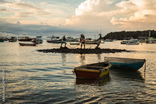 Photos Horizontal view of Three fishermen (Tres pescadores) sculpture and boats at Buzios beach, Brazil during dusk on a cloudy summer day