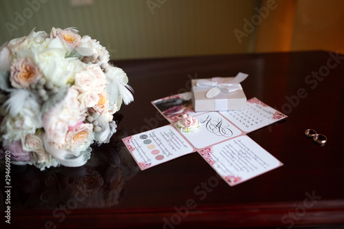 Wedding bouquet of peonies and roses lying on a wooden vintage table near wedding rings on the background of the invitation in the apartments to prepare the bride and expectation of the groom.