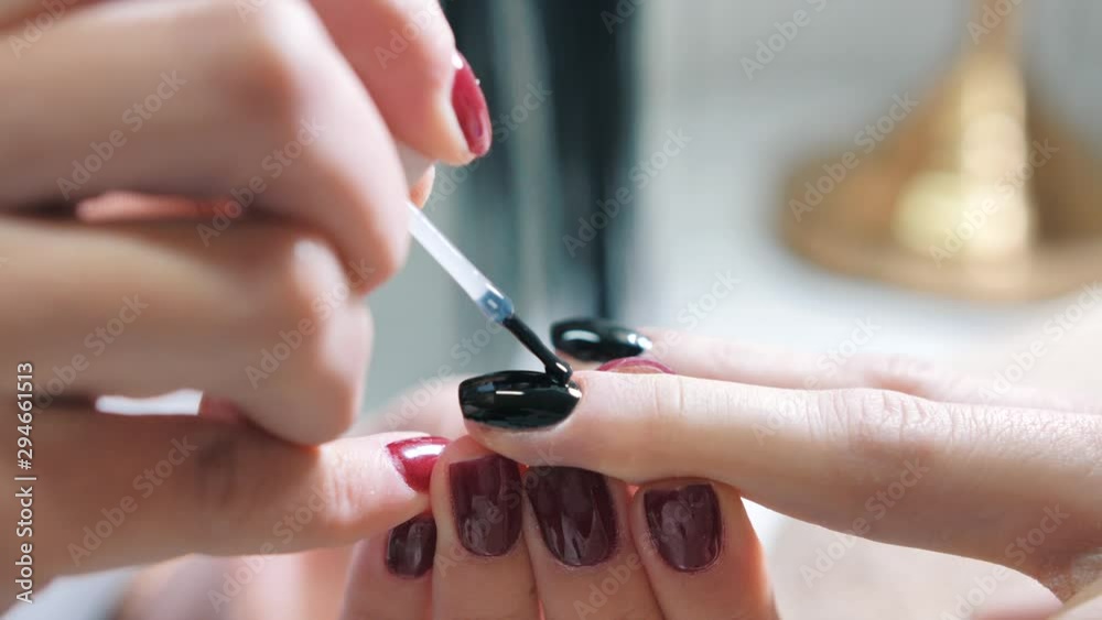 A close up view of a beautician applying black color nail paint on the nails of a customer during manicure session.A static footage.Concept of beauty,self care,professionalism,fashion.