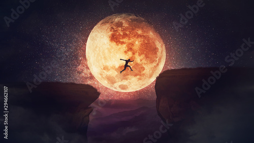 Surreal scene, self overcome concept, as determined man jump over a chasm obstacle. Way to win and success over starry night with full moon background. Motivation for achieving goals. photo