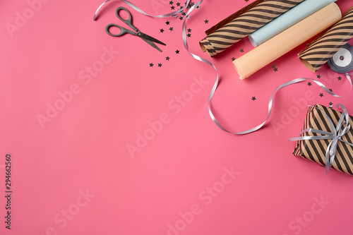 Striped brown gift box tied with silver ribbon on a pink background. Wrapping paper and scissors are laying nearby. Close-up, copy space, top view.