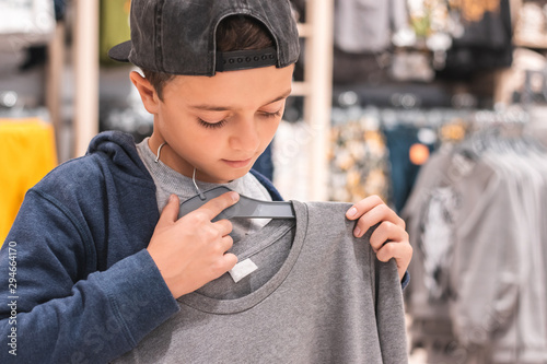 Young boy choosing clothes in the shop by himself, putting on new looks, checking for style. Shopping, black friday, discount and sales concept. photo