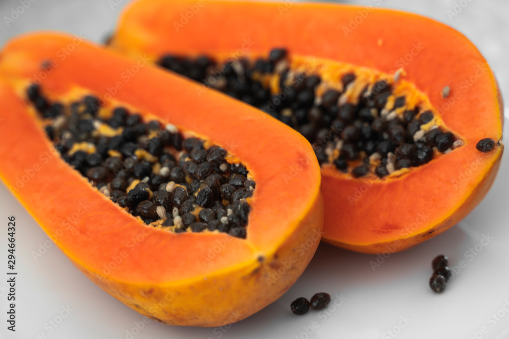 Half cut ripe papaya with seed on a white plate. Slices of sweet papaya with a white background. Halved papayas. Healthy exotic fruits. Vegetarian food. Half cut ripe papaya with seed on a white plate. Slices of sweet papaya with a white background. Halved papayas. Healthy exotic fruits. Vegetarian food.