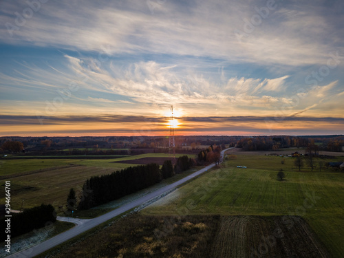 Drone photo of empty road leading through the rural village, towards the sun - colorful autumn sunset