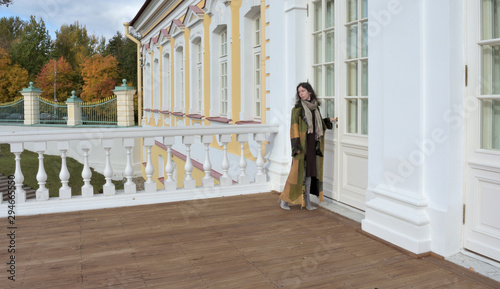 young beautiful pretty lady woman posing in a long green and brown dress gown overcoat on terrace and steps of historical palace in Oranienbaum near Saint Petersburg, Russia