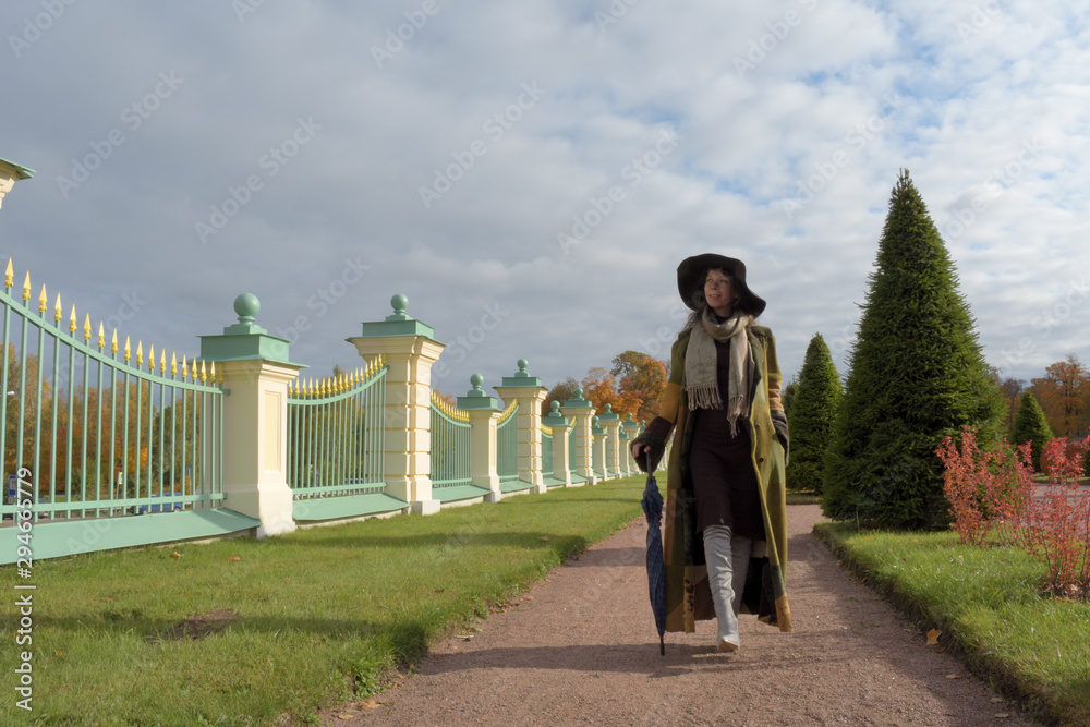 young beautiful pretty lady woman in a long green and brown dress gown overcoat walks in the garden of the palace in Oranienbaum near Saint Petersburg, Russia on a sunny beautiful autumn day
