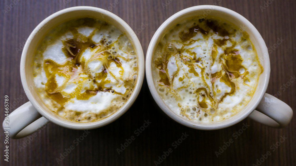Two cups of cappuccino with latte on wooden background. Beautiful foam, white ceramic cups, stylish toning. Drinking coffee to start a day positive or stay awake. Coffee addiction concept. Two cups of cappuccino with latte on wooden background. Beautiful foam, white ceramic cups, stylish toning. Drinking coffee to start a day positive or stay awake. Coffee addiction concept.