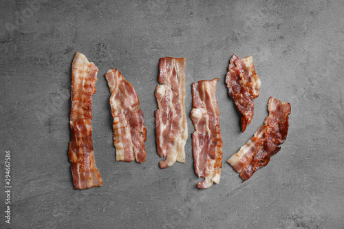 Slices of tasty fried bacon on dark background, flat lay
