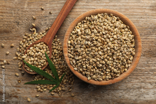 Organic hemp seeds and leaf on wooden background, flat lay