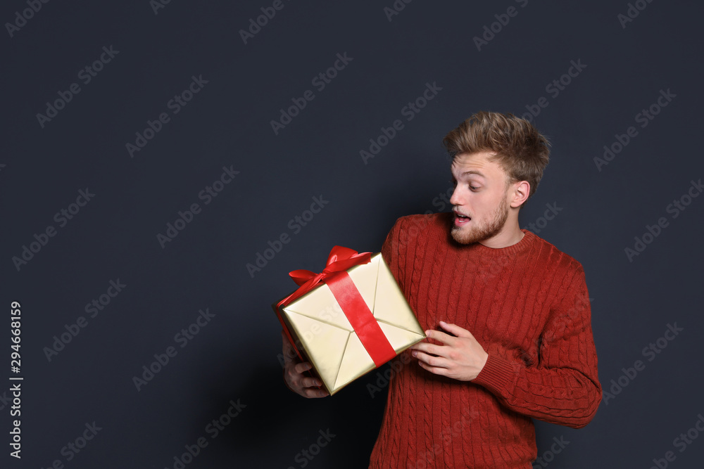 Emotional young man with Christmas gift on dark background. Space for text Emotional young man with Christmas gift on dark background. Space for text