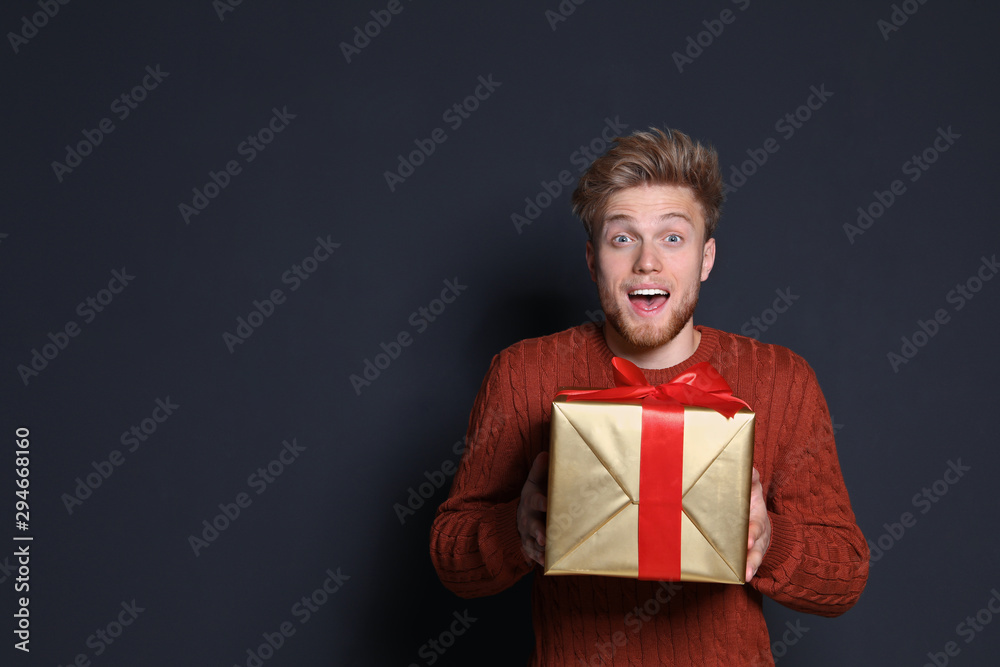 Emotional young man with Christmas gift on dark background. Space for text Emotional young man with Christmas gift on dark background. Space for text