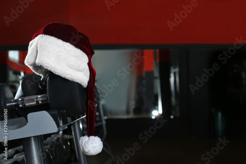 Santa hat on stand with dumbbells in modern gym. Space for text