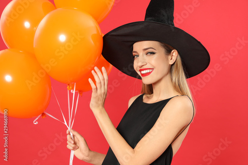 Beautiful woman wearing witch costume with balloons for Halloween party on red background