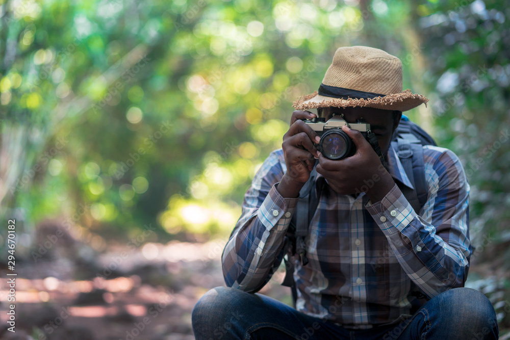 African freedom man traveler holding camera with backpack standing in the green natural forest.