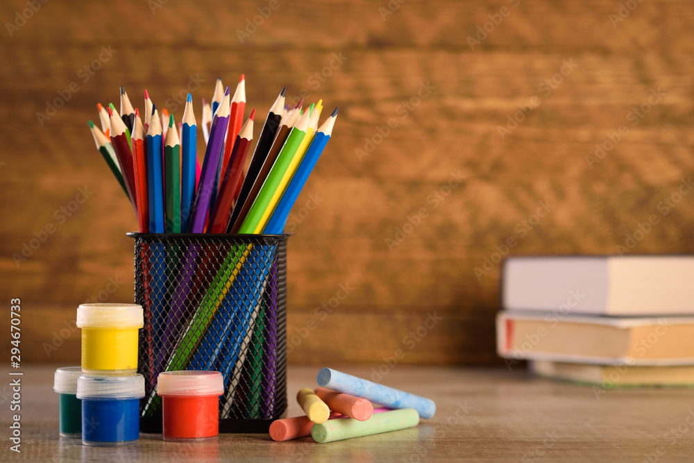 School supplies on a warm, beautiful wooden background. Colored children's pencils in a locker black holder for stationery. School supplies on a warm, beautiful wooden background. Colored children's pencils in a locker black holder for stationery.