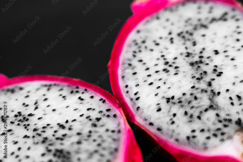 Obraz premium Dragon fruit. Vibrant Dragon Fruit on black background. Sliced white dragon fruit or pitaya on black plate on the table, close-up. Tropical and exotic fruits. Healthy and vitamin food concept.