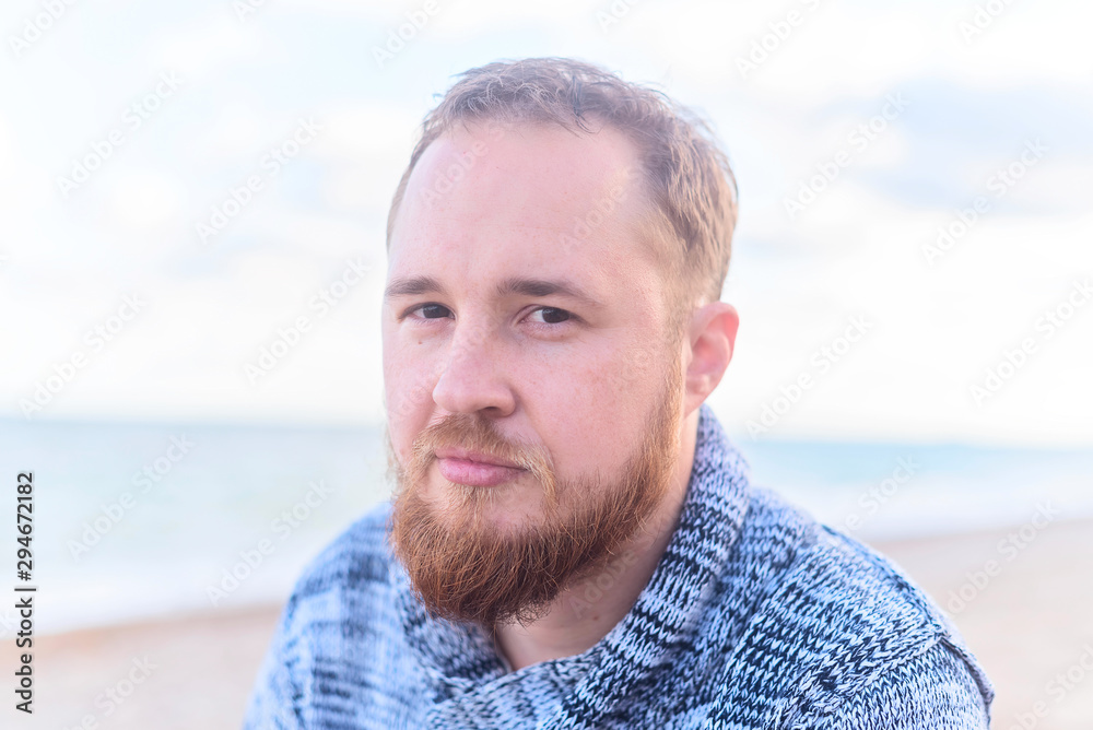 Portrait of a bearded red-haired man in sweater with freckles on the background of the sea Portrait of a bearded red-haired man in sweater with freckles on the background of the sea