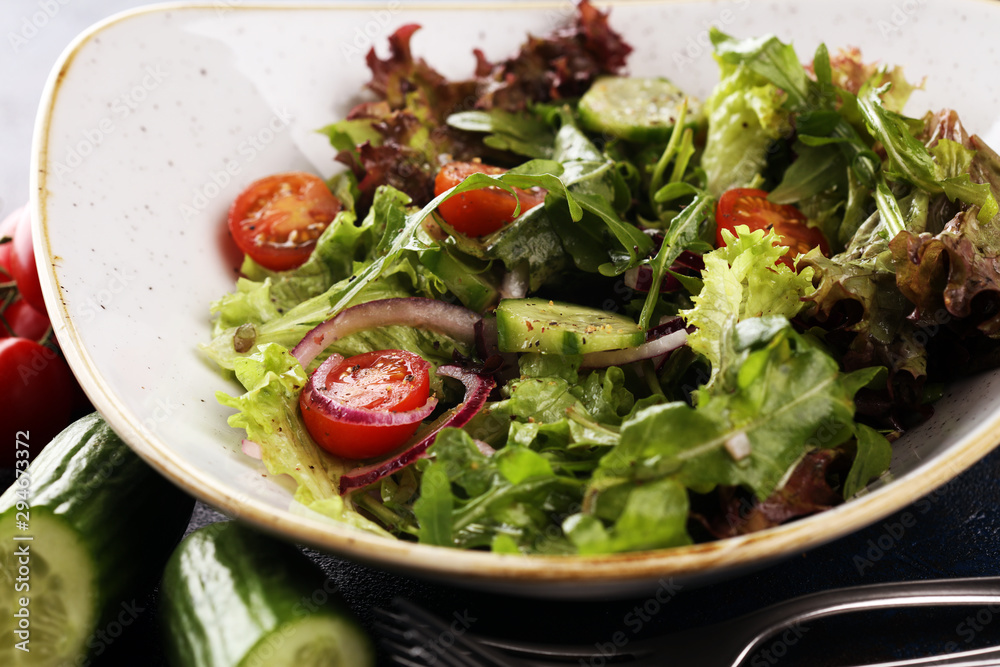 bowl of salad with vegetables and greens, with tomato, cucumber and onions on rustic table bowl of salad with vegetables and greens, with tomato, cucumber and onions on rustic table