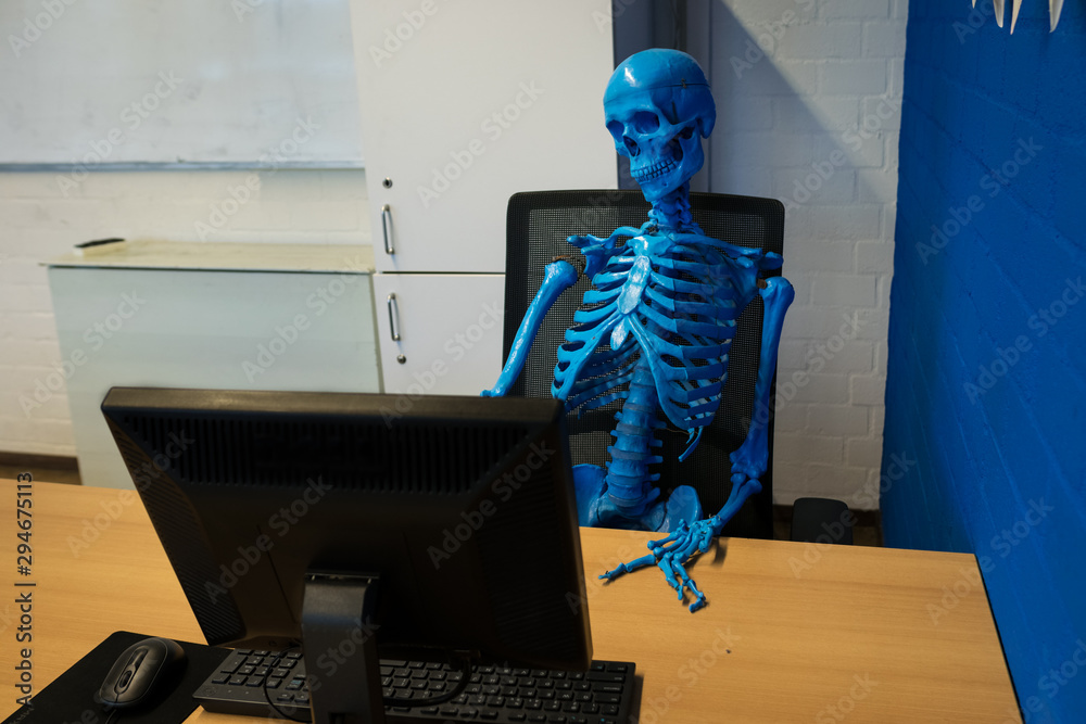 Skeleton sitting behind computer desktop. Persiflage on lifestyle of ...