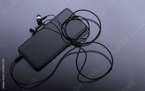 black smartphone with black headphones on glass surface