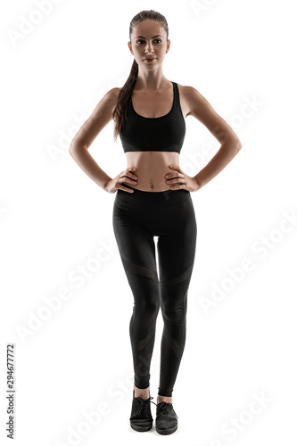 Brunette woman in black leggings, top and sneakers is posing isolated on white. Fitness, gym, healthy lifestyle concept. Full length.
