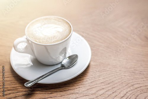 White cup of coffee with art on wooden table with copy space.