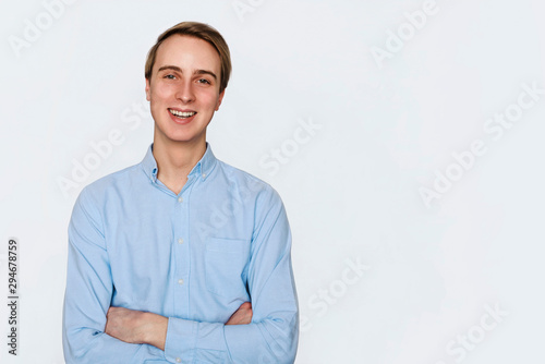 Portrait of young confident charismatic young male in blue t-shirt holding hands crossed on chest. Self-assured, smiling and laughing as looking friendly at camera. Isolated. Add your text. © YM studio